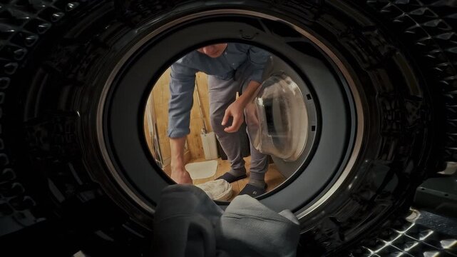A man loads soiled laundry into a laundromat washer, adding detergent, and initiates the cleaning cycle, simplifying household chores and freshening fabrics in a public laundry facility