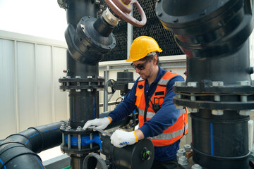 Fototapeta premium Industrial worker in hard hat and safety vest tightens pipe fitting with wrench on machinery