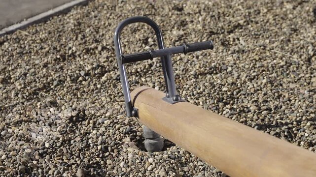 Minimalist seesaw with long wooden log and handles on playground closeup. New empty teeter totter for kids amusement in sunny park