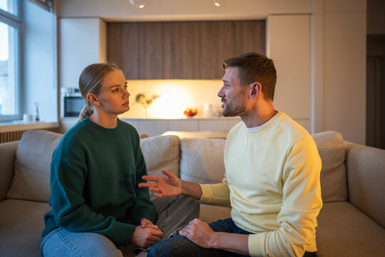 Lying toxic husband creating stories and manipulates facts about love affair, man telling lies to wife sitting on couch in room, cheating male playing guilty and tries to escape break up with spouse.