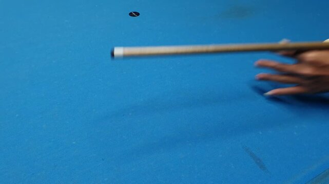 Close-up of a hand gripping a cue stick on a vibrant blue pool table, emphasizing game strategy and focus in a recreational setting.