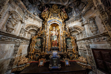 Baroque retablo with Virgin and Child stands in Seville, Spain. Warm light reveals gold leaf, cherubs, ornate columns, carved stone walls, lamps, and portrait medallions.