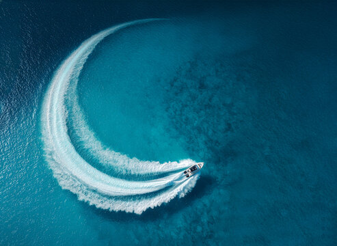 Drone aerial view of a speedboat creating a crescent moon wave in clear blue ocean water, symbolic Ramadan and Eid concept with travel tourism, marine adventure, and luxury boating lifestyle