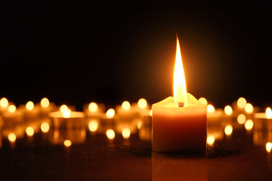 Burning candles as a symbol for religion or mourning in times of war. One large candleflame in front of defocused flames in the dark and black background.