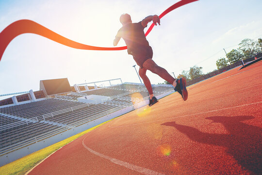 Fit young male running sprinting to red finish line at the racetrack. Finisher, marathon runner sprinting moment at the racetrack.	