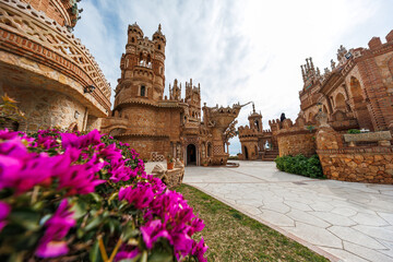 Ornate turrets and brickwork rise over a courtyard in Benalmadena, Malaga. Magenta bougainvillea, Mediterranean beyond arches, ship sculpture, Gothic and Mudejar motifs. © True Pixel Art