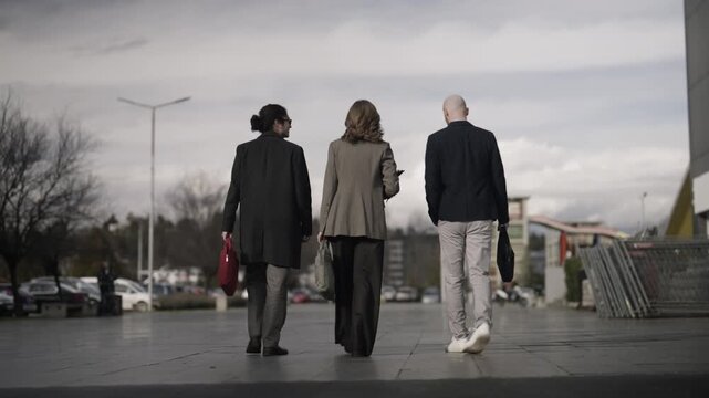 Three diverse business people walk away from the camera in an urban environment. This group of professionals is heading to a corporate meeting.
