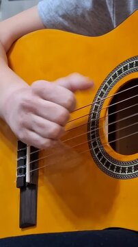 Student learns to play guitar, focusing on right-hand finger placement and plucking. Classical guitar with a decorative rosette and vibrant yellow finish. Concept of music education and creativity