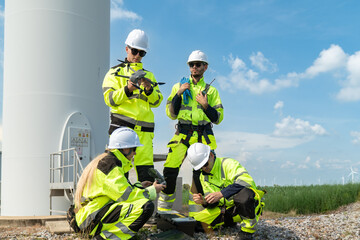 Fototapeta premium Team of engineers using drone for wind turbine inspection at wind farm. Professional industrial workers with remote control for renewable energy project monitoring, smart technology sustainability