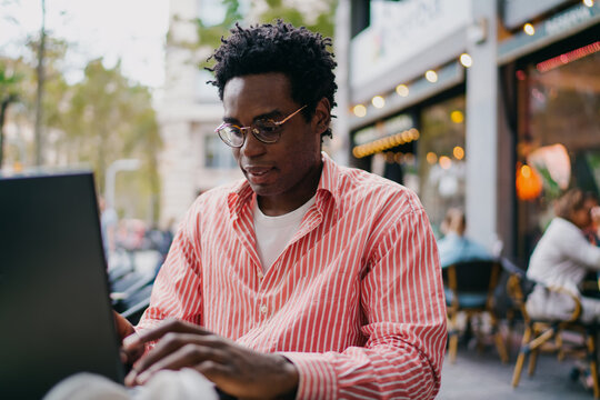 Freelancer typing on laptop in outdoor caf&eacute;, isolated and focused on screen, symbolizing independence, remote productivity and tech-based creative workflow.