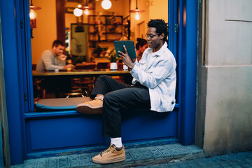 Side profile of man holding tablet with stylus in cozy cafe environment, highlighting individual focus, content consumption, and personal tech immersion.