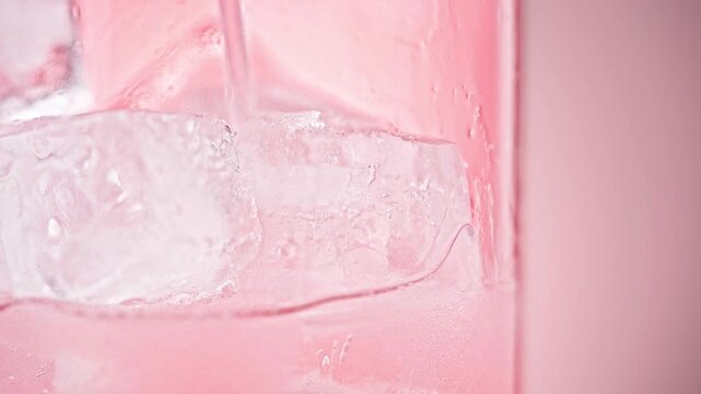 Macro Close-up of Pink Liquid Pouring into a Glass with Ice Cubes on Pink Background, Refreshing Summer Drink Advertising