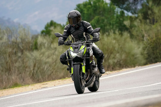 Motociclista con equipamiento completo conduciendo una motocicleta "naked" verde y negra en una carretera de monta&ntilde;a con curvas.
