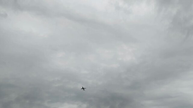 Silhouette of lone commercial jet soa ring through vast expanse of grey overcast clouds. Dark aircraft against moody sky. Passenger airplane flying steadily. Long-distance air travel, logistics