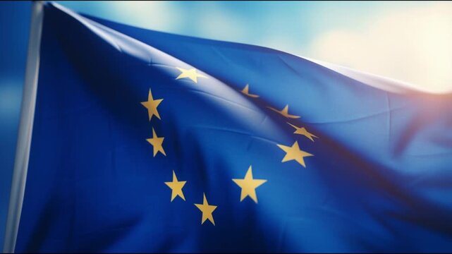 Close-up of the European Union flag waving in the wind, its blue fabric and golden stars illuminated by sunlight against a clear sky. Symbolic concept of unity, democracy, and international alliance.