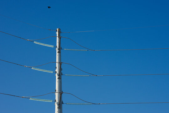 High-voltage power lines attached to a concrete utility pole with glass insulators set against a clear blue sky, highlighting electricity infrastructure, energy distribution and minimalist industrial 