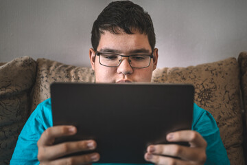 teenager in glasses looks intently at a tablet screen, focused on the display. © diy13
