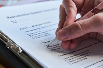 Close up of hand holding pen filling out reproductive system questionnaire on clipboard, marking...