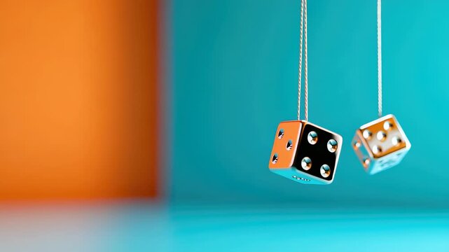 Two silver dice hanging from strings against orange and green split background
