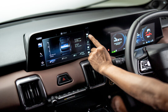 Hand operating infotainment touchscreen inside electric vehicle showing energy usage and driving range on digital dashboard display.
