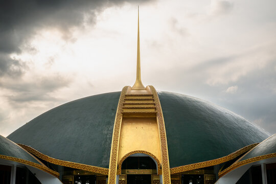 Majestic green mosque with multiple domes under a cloudy sky viewed from a low angle. The mosque with green and brass domes, is designed in the Islamic architectural tradition in Jember, Indonesia.