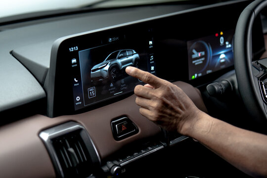 Close up of driver hand interacting with infotainment touchscreen displaying car interface and connectivity features inside modern vehicle dashboard.

