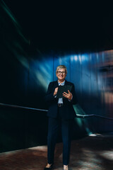 Smiling senior businesswoman using digital tablet in dark modern space. Scene conveys confidence,...