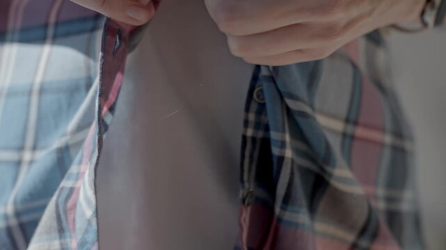 Closeup of woman hands unbuttoning button on plaid shirt