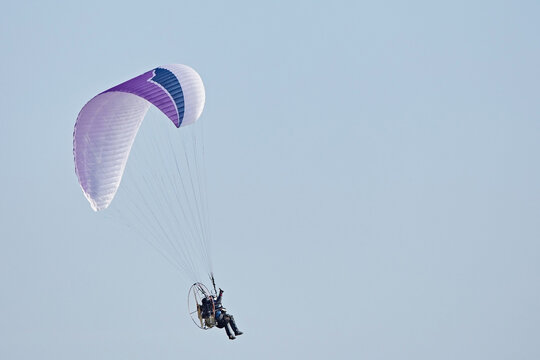 A motorized paraglider flies through the sky