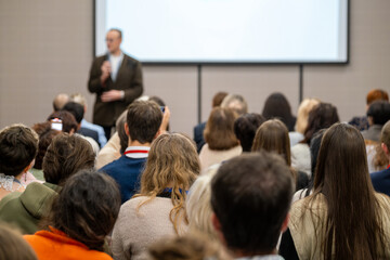 Audience listening to speaker at conference, people attending presentation in meeting room with projection screen. © Anton Gvozdikov
