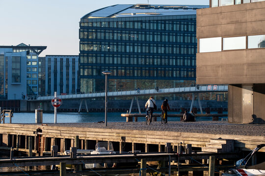 Modern glass office building facing a waterfront promenade and pier in Copenhagen Denmark with people walking through an urban business district