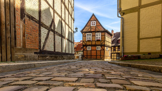 Traditional half-timbered house and narrow cobblestone street in the UNESCO World Heritage old town of Quedlinburg, Germany. Medieval German architecture under a bright blue summer sky.