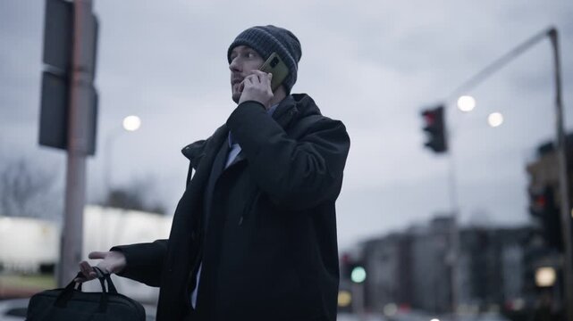 A young business professional communicates on his smartphone in an urban environment. He appears focused during his outdoor phone call.