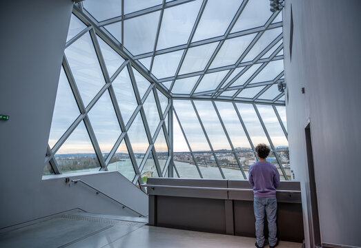 Lyon, france. December 28, 2023. Person standing inside mus&eacute;e des confluences in lyon, looking out at the city and river through the geometric glass roof