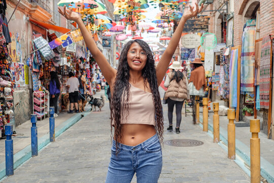 Young Latina woman on vacation with her hands up in the colorful streets of the city of Apz in Bolivia - travel concept