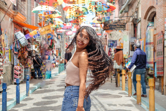 Young Latina woman with dark skin on vacation, her hair blowing in the wind on Calle de las Brujas in the city of Apz in Bolivia - travel concept