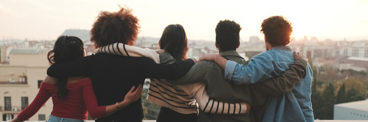 Fototapeta premium Guys and girls at the party, looking at the beautiful views and talking standing on the terrace, friendly party holiday at sunset. Panoramic