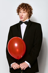 Obraz premium Curly young man celebrates his birthday in a stylish tuxedo with a cheerful balloon