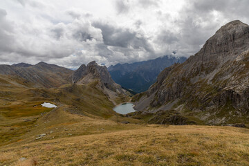 Obraz premium Scenic mountain view from Col de la Ponsonnière, Cerces Massif, overlooking alpine slopes and the alpine Grand Lake below under a cloudy sky