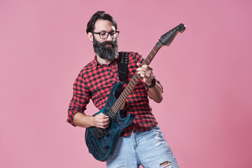 Naklejka premium Bearded man playing electric guitar in a studio against a pink b
