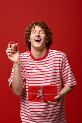 Obraz premium Stylish young man joyfully holding gifts in a vibrant red studio setting