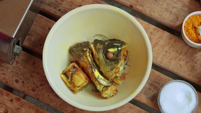 Top view of marinating fish heads with turmeric and salt in a bowl for traditional South Asian cooking.