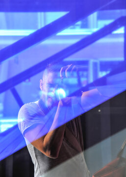 reflection of a man taking a photo through a glass window with abstract blue light streaks. The image shows urban geometry and creative self-portrait style. Concept of photography