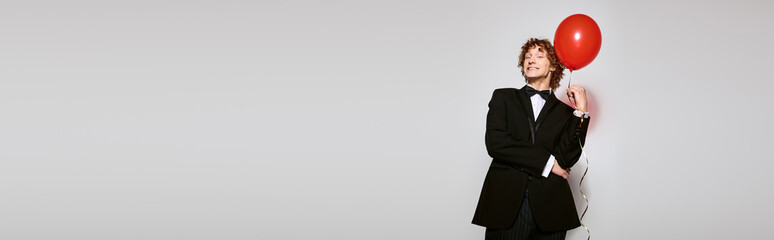 Obraz premium Curly-haired young man celebrates birthday in elegant tuxedo with a vibrant balloon