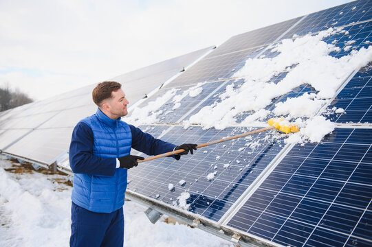 Worker cleaning snow from solar pannels in winter
