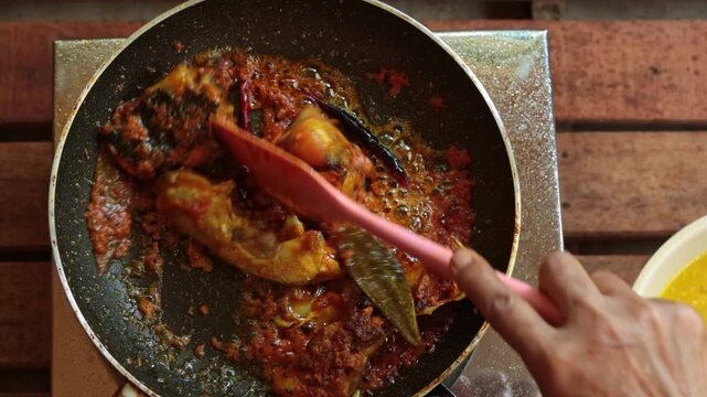A cinematic, top-down shot of authentic Indian fish curry (Macher Jhol) simmering in a vibrant, spicy red gravy. The video captures the cooking process in a non-stick pan.
