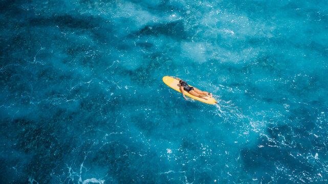 Woman on surfboard in blue sea. Drone view of surfer during surfing