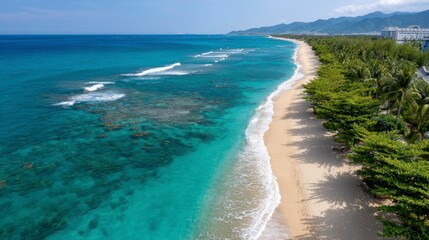Coastline shows turquoise ocean waves hitting sandy beach with city buildings and mountains far away under clear skies