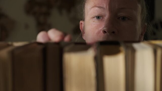Woman reader choosing and taking book from bookshelf close-up, view from inside bookcase