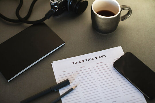 Close-up of a To do list, notebook, pens, mobile phone, camera and a cup of black coffee on a desk